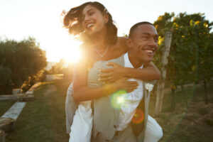Workplace-romance.-Happy-man-giving-piggyback-ride-to-bride-in-farm-at-wedding-during-sunset.