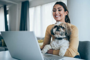 Female-employee-working-on-laptop-while-her-dog-sits-in-her-lap. 