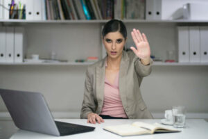 Portrait-of-female-employee-sitting-at-her-office-desk-and-gesturing-the-stop-sign-with-her-palm.
