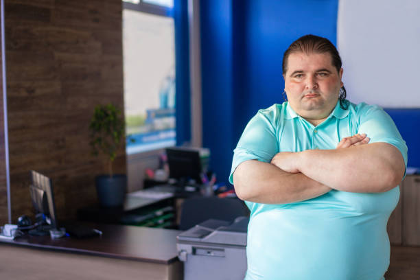 A-large-overweight-employee-standing-with-his-arms-crossed-in-the-middle-of-an-office.-When-fat-shaming -gets-you-dismissed.